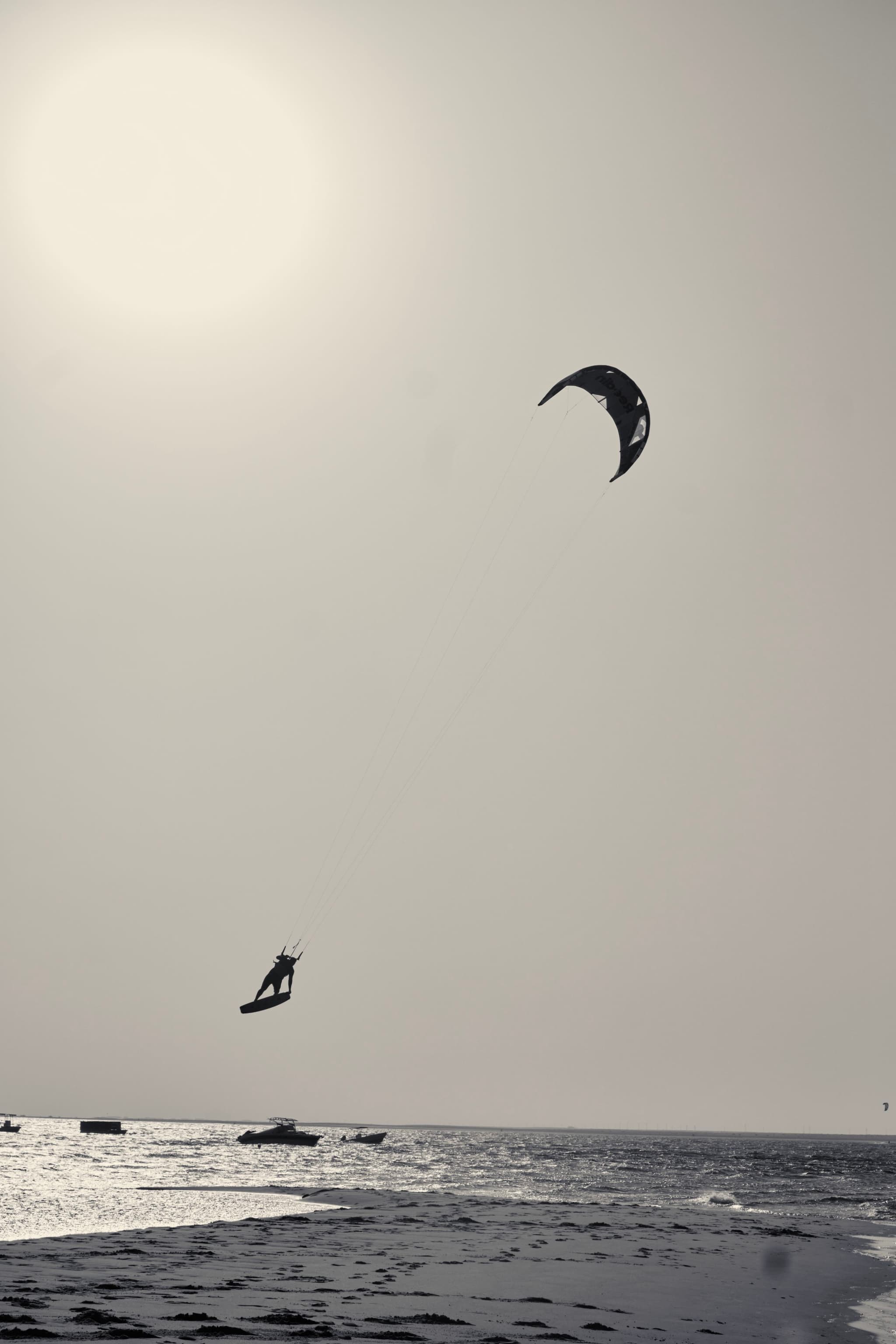 A person kite surfing over the ocean with a bright sun in the sky, creating a silhouette effect