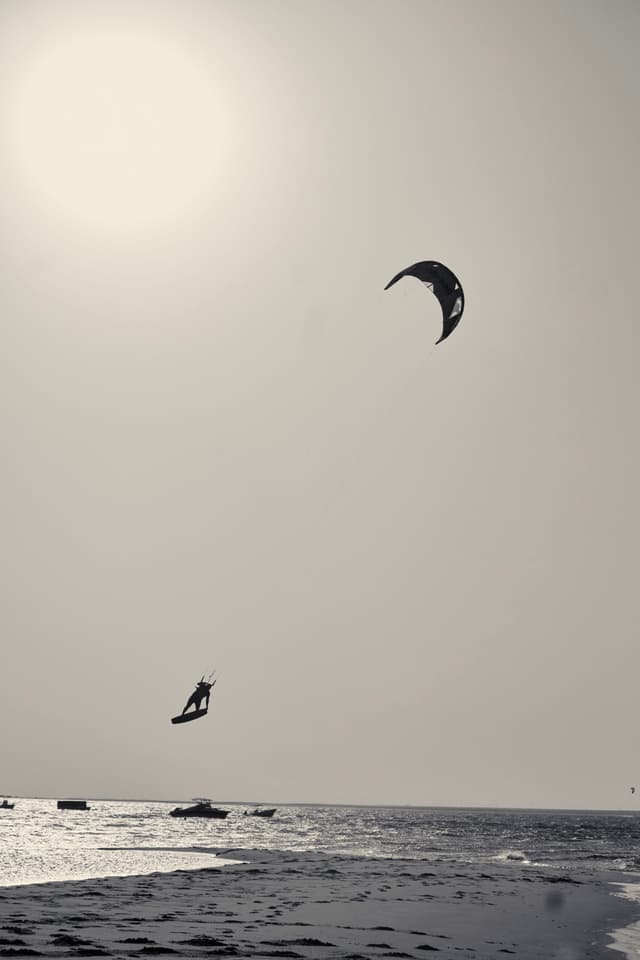 A person kite surfing over the ocean with a bright sun in the sky, creating a silhouette effect