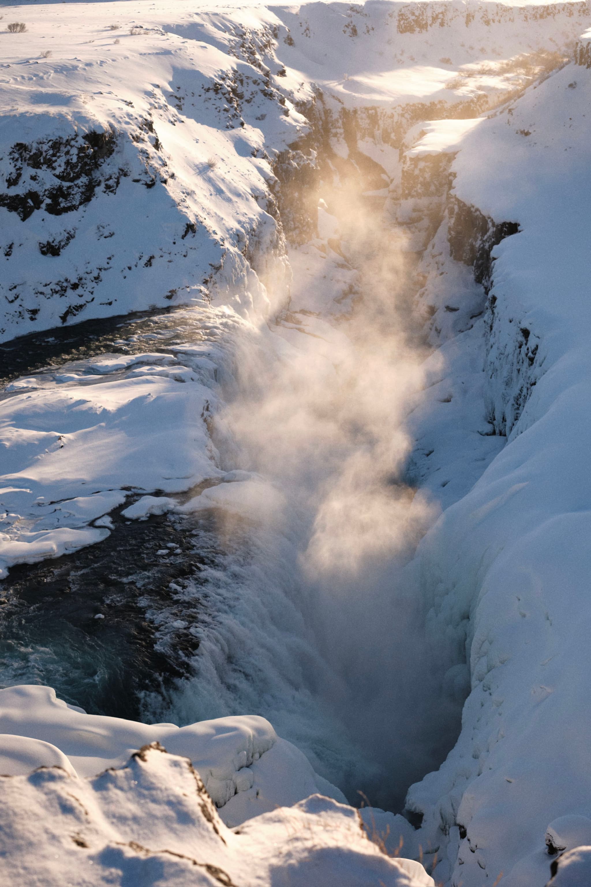 A waterfall surrounded by snow-covered cliffs, with mist rising from the cascading water