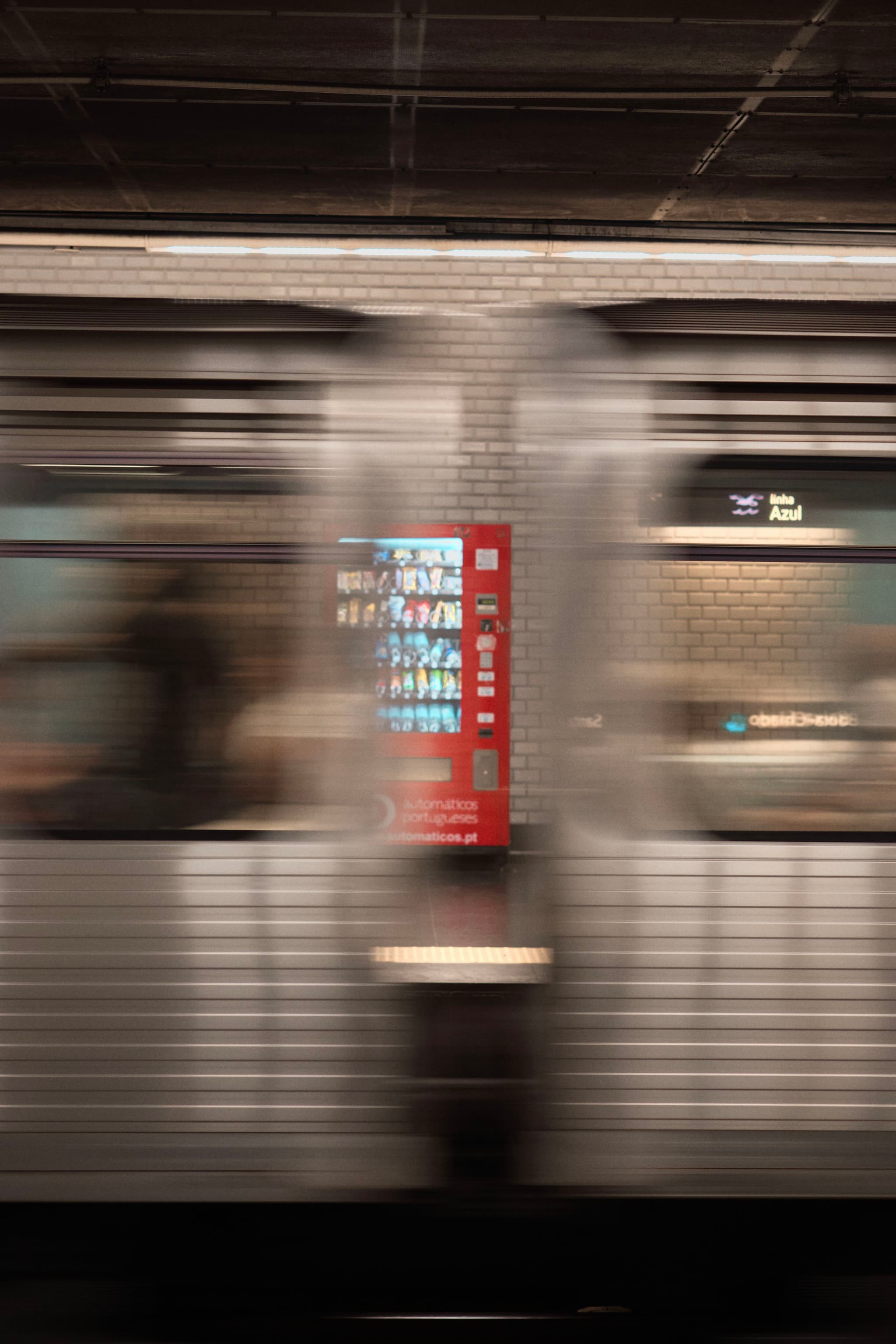 A blurred subway train in motion with a red sign and tiled wall in the background