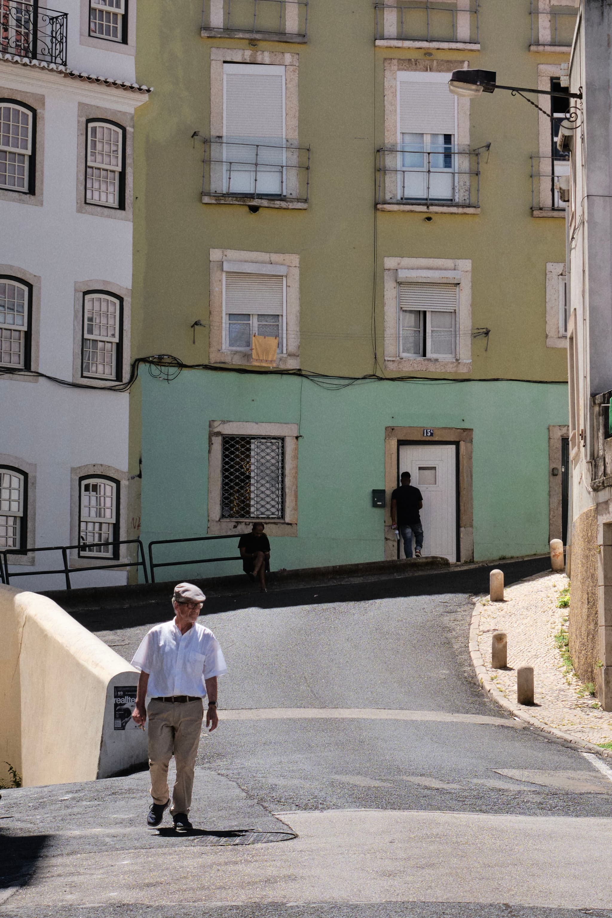 A man walks down a sunlit street with pastel-colored buildings in the background