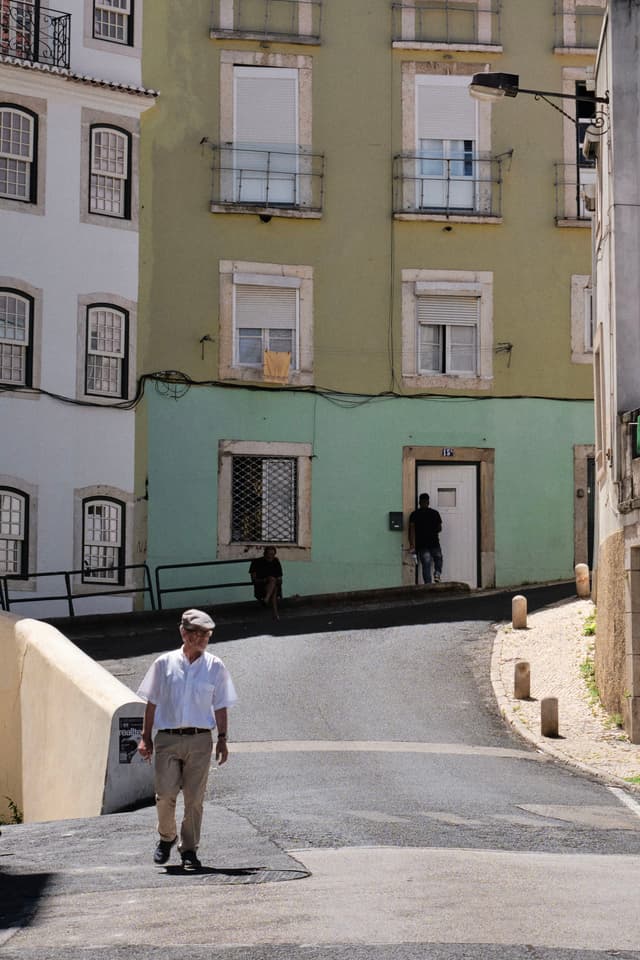 A man walks down a sunlit street with pastel-colored buildings in the background