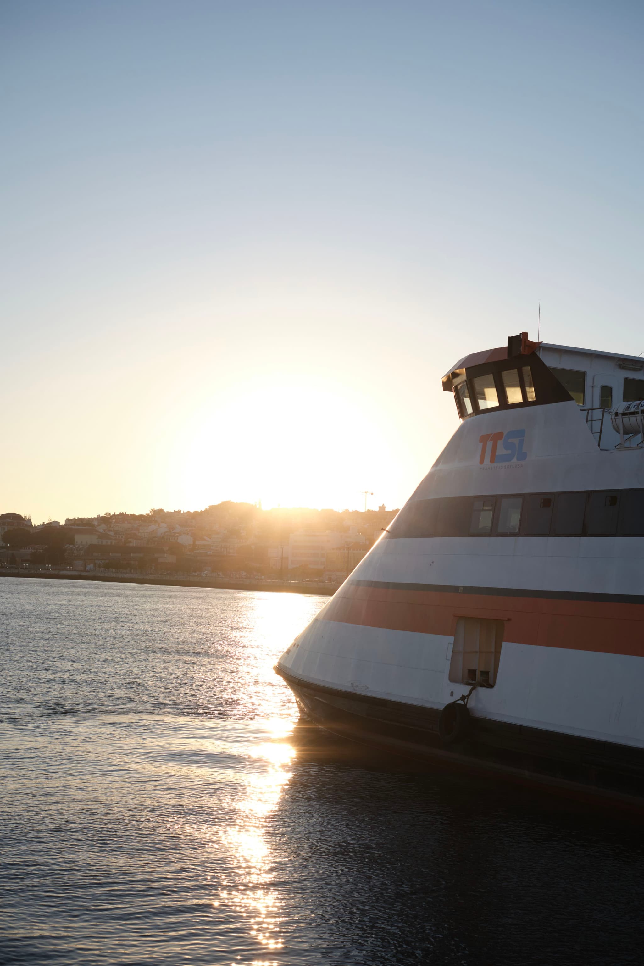 A ferry on the water with the sun setting in the background, casting reflections on the surface