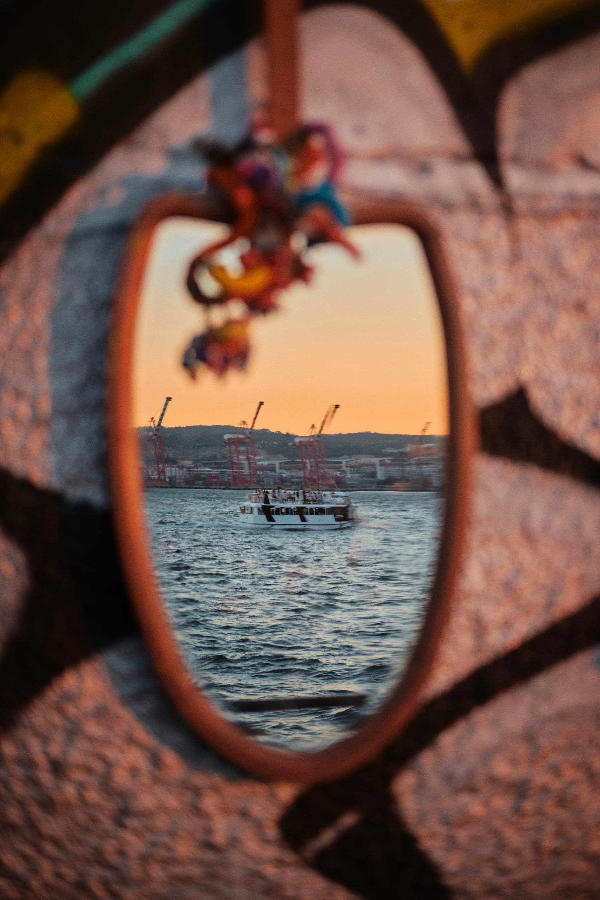 A mirror hanging on a graffiti-covered wall reflects a serene waterfront scene with boats and cranes at sunset