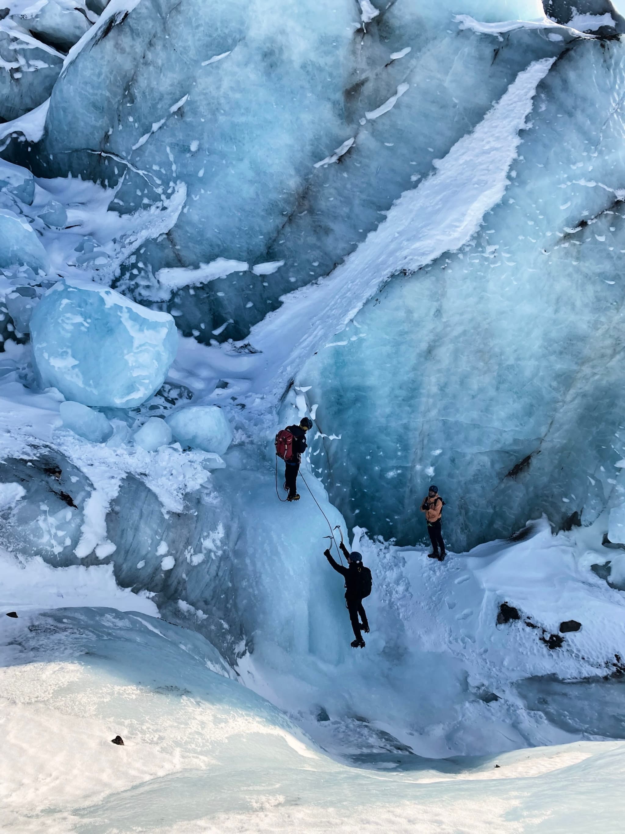 Three people are climbing a large, icy glacier with visible blue ice formations