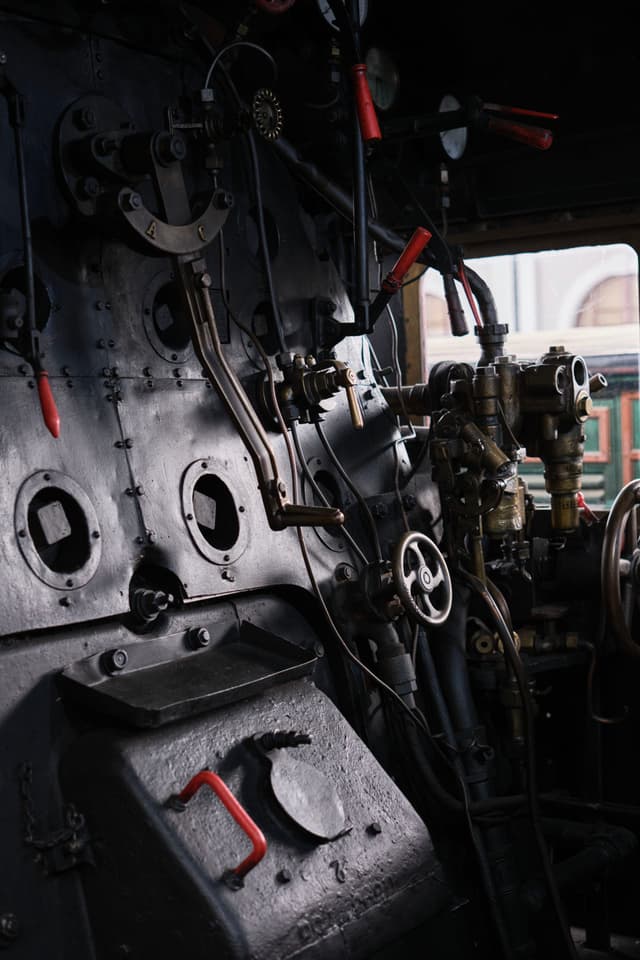 The interior of a vintage steam locomotive cab with various levers, gauges, and valves