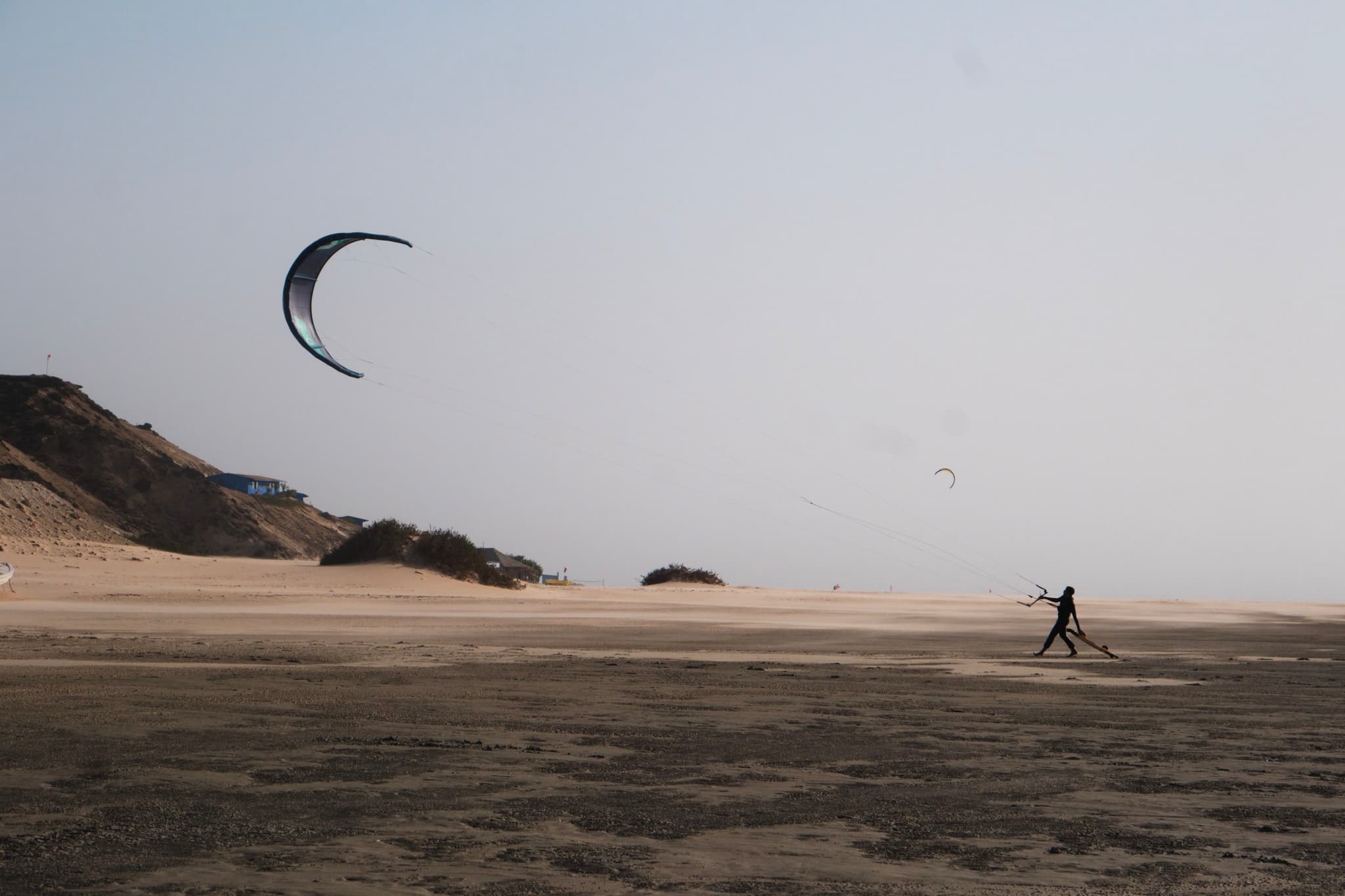 A person kite flying on a sandy beach with dunes in the background