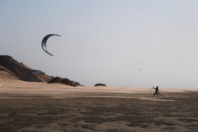 A person kite flying on a sandy beach with dunes in the background