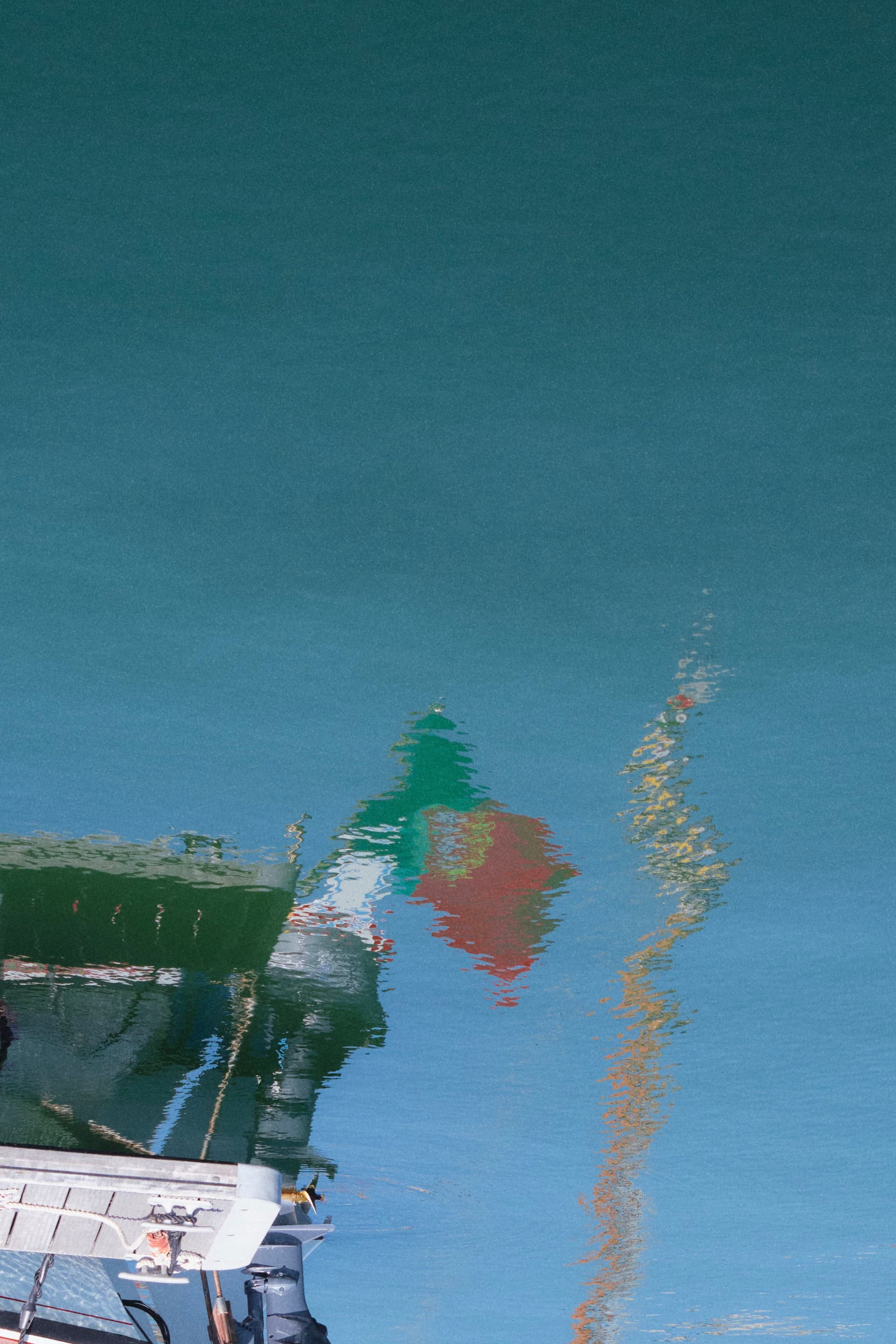 A reflection of a boat and a flag in calm water, with the flag's colors appearing as green, white, and red
