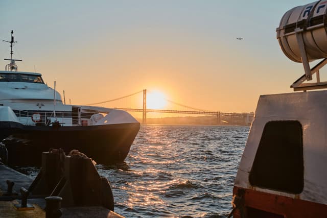 A sunset over a body of water with a bridge in the background, boats in the foreground, and gentle waves