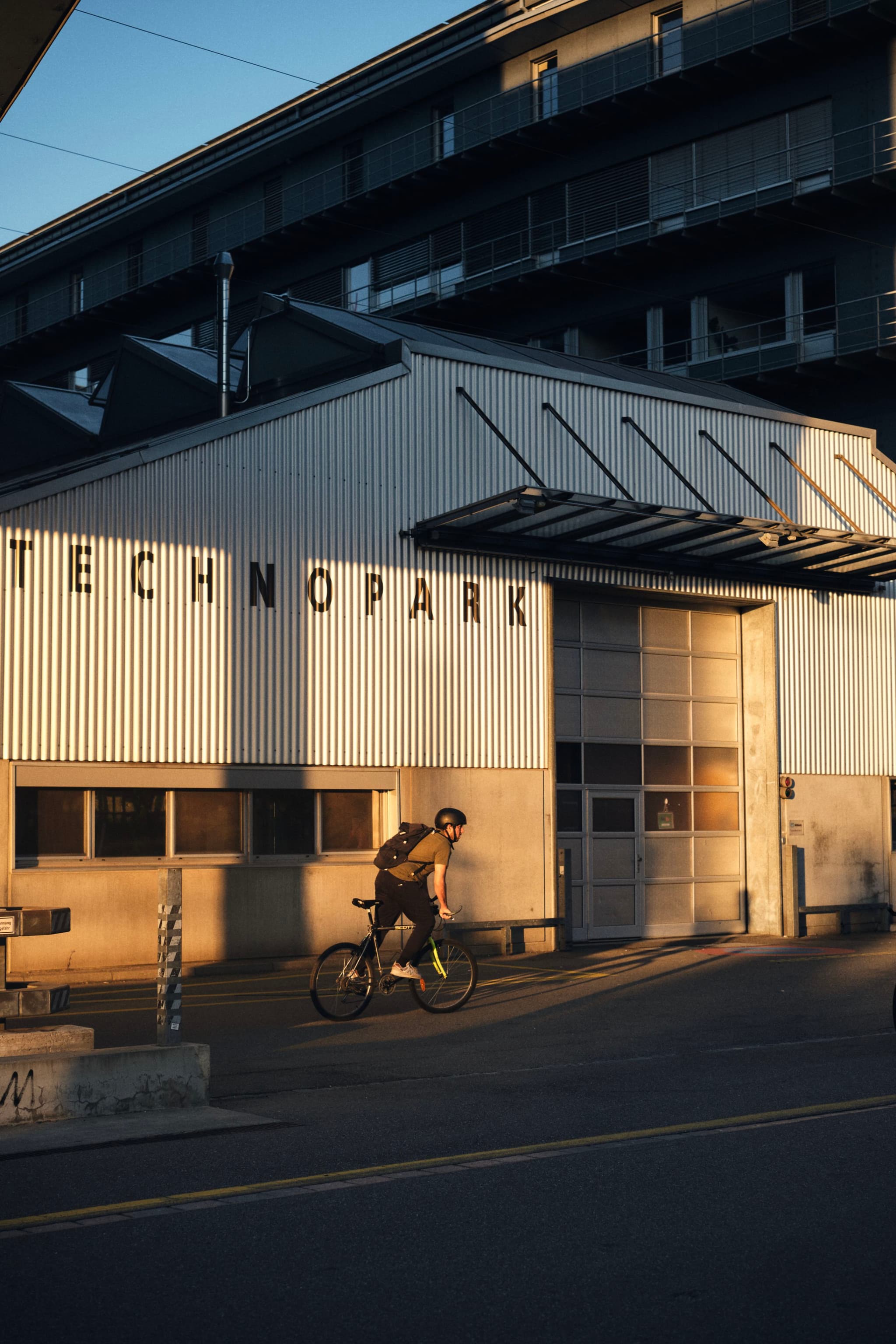 A cyclist rides past a building labeled TECHNOPARK in the warm glow of sunset