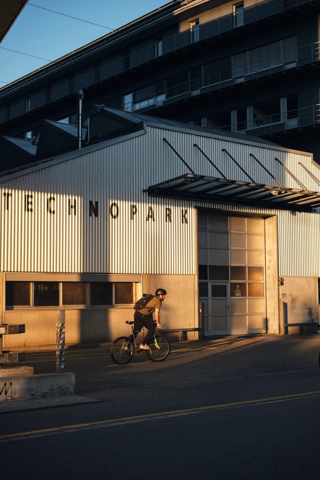 A cyclist rides past a building labeled TECHNOPARK in the warm glow of sunset
