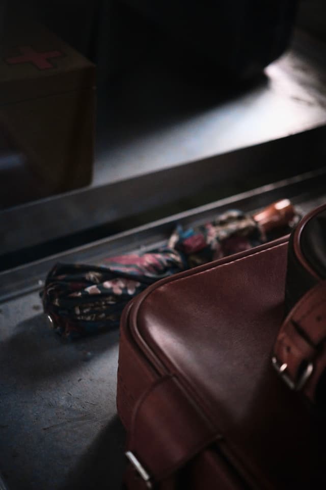 A close-up of a brown leather bag and a folded umbrella with a colorful pattern, placed on a reflective surface