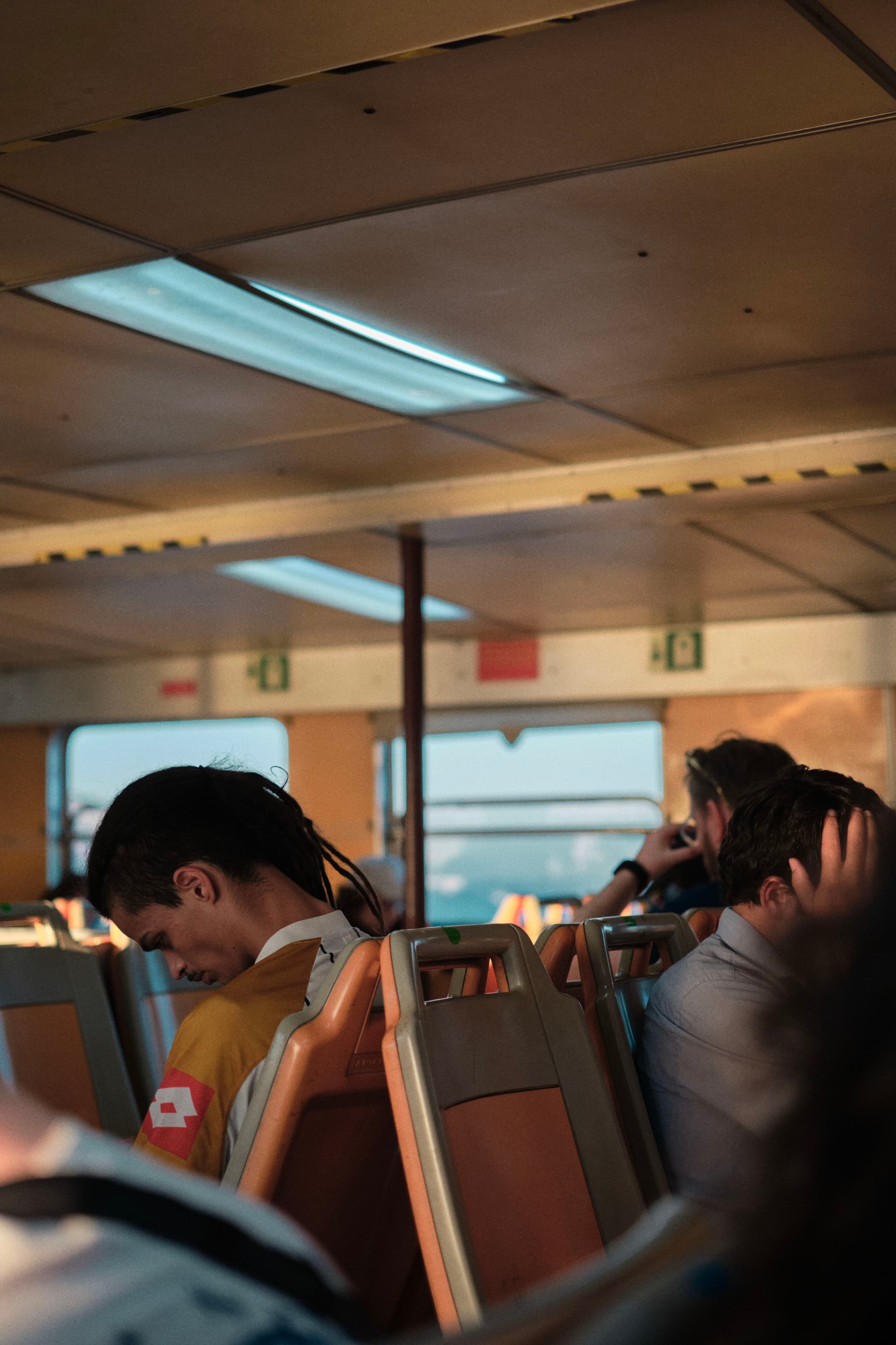 Passengers seated inside a ferry, with overhead lighting and windows in the background