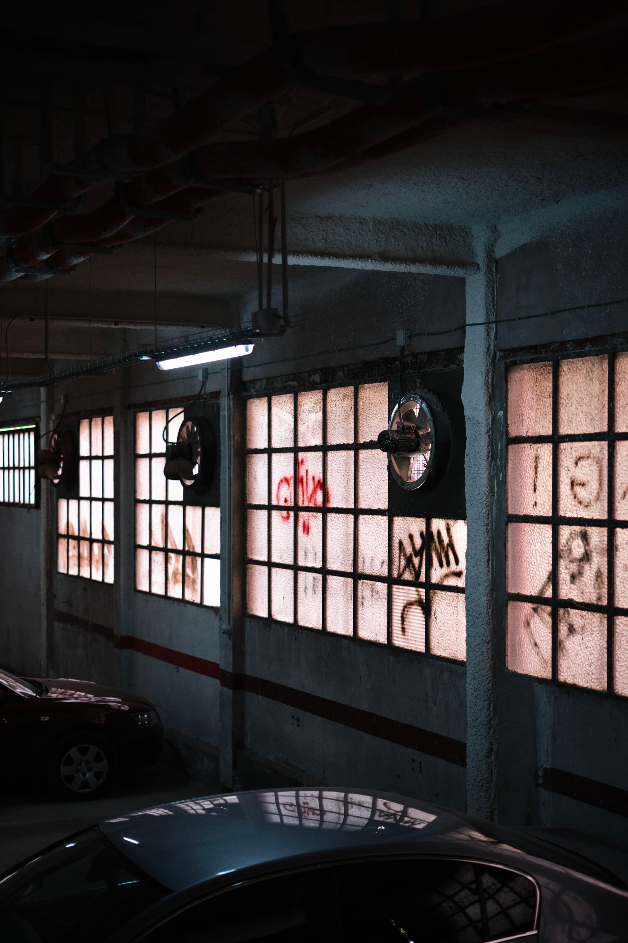 A dimly lit parking garage with graffiti-covered windows and parked cars