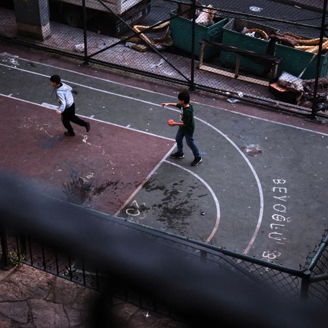 Two people running on a wet, outdoor basketball court with a fence and some debris in the background