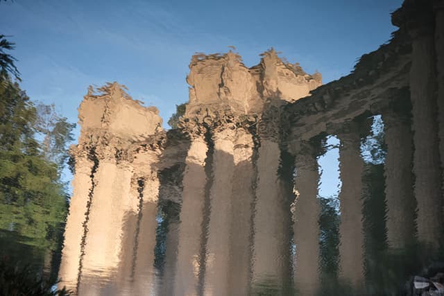 Ancient-style columns reflected in water, creating a distorted, wavy appearance