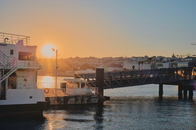 A waterfront scene at sunset with boats docked near a pier and a cityscape in the background