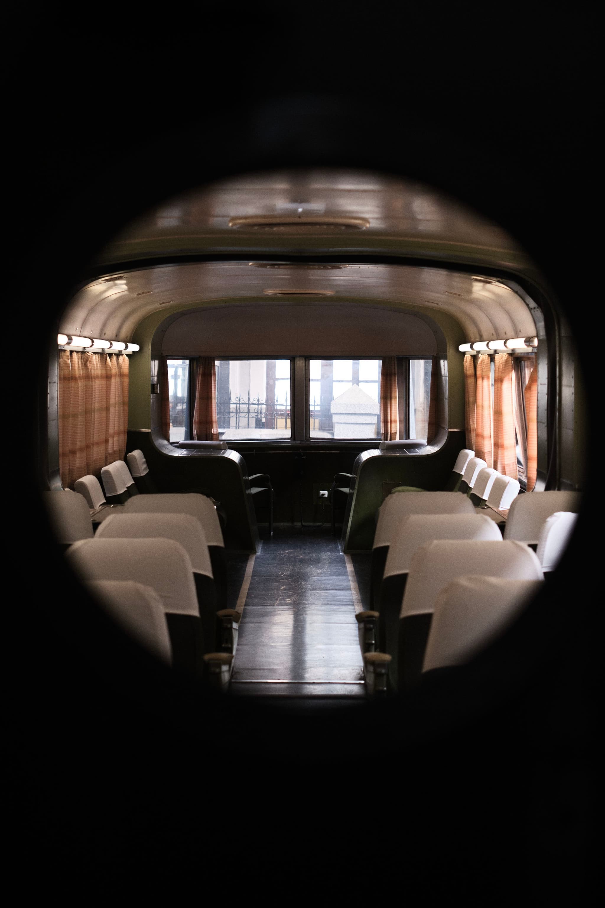 A vintage train car interior with rows of white seats and large windows at the end, viewed through a circular frame