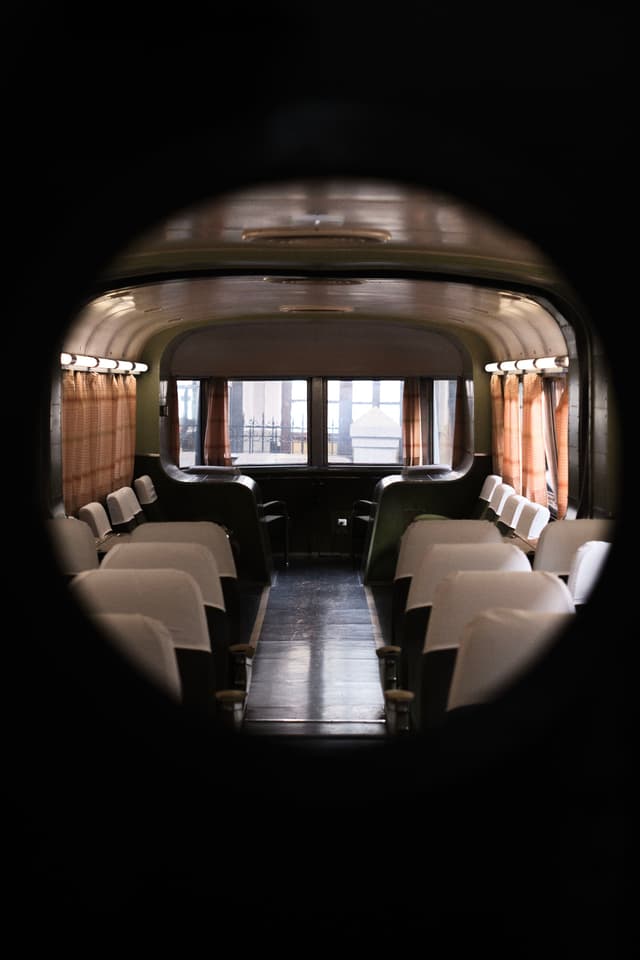 A vintage train car interior with rows of white seats and large windows at the end, viewed through a circular frame