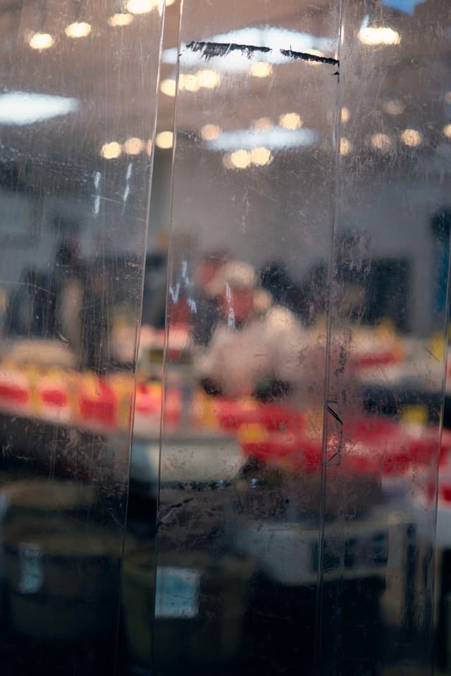 A blurred view through a glass panel, revealing a busy indoor setting with people and colorful objects in the background