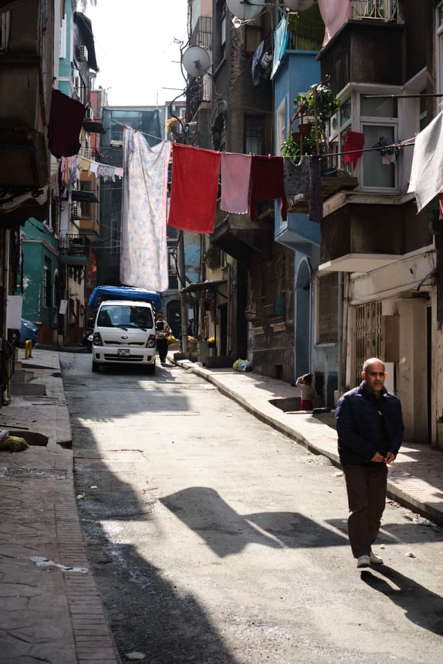 A narrow urban street with laundry hanging between buildings, a white van parked, and a person walking